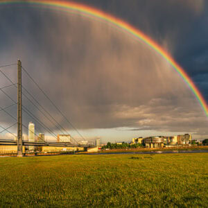 Fine-Art-Print Regenbogen über dem Rheinturm in Düsseldorf bei Unwetter – Panorama mit Rheinwiesen, Brücke und dramatischem Himmel, erhältlich als hochwertiger Kunstdruck.