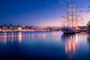 Fine-Art-Print Stockholm Skyline mit beleuchtetem Segelschiff bei Sonnenuntergang, erhältlich als hochwertiger Kunstdruck.