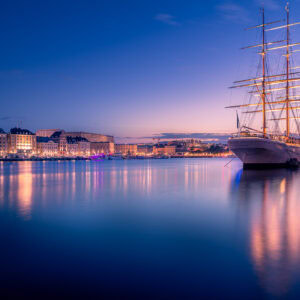 Fine-Art-Print Stockholm Skyline mit beleuchtetem Segelschiff bei Sonnenuntergang, erhältlich als hochwertiger Kunstdruck.