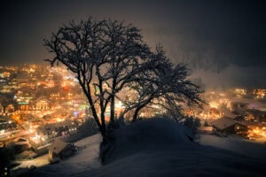 Verschneiter Baum mit Blick auf die Lichter von Wolkenstein bei Nacht – erhältlich als Fine Art Print