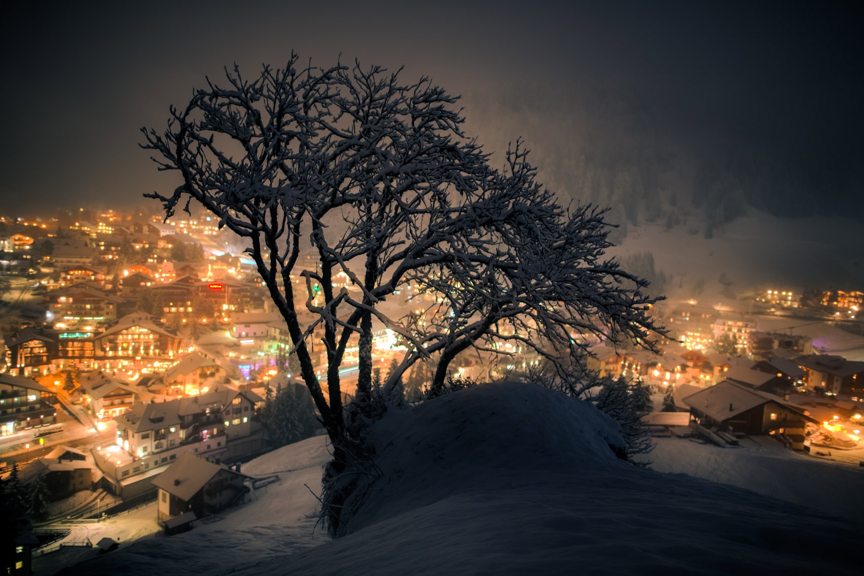 Verschneiter Baum mit Blick auf die Lichter von Wolkenstein bei Nacht – erhältlich als Fine Art Print