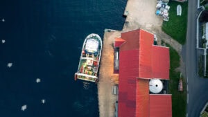 Fine-Art-Print Luftaufnahme Bootsanleger mit rotem Dach auf der Insel Hidra in Norwegen, erhältlich als hochwertiger Kunstdruck