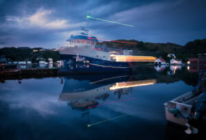 Fine-Art-Print Boot mit Lichtspuren auf spiegelglattem Wasser bei Nacht in Hidra, Norwegen, erhältlich als hochwertiger Kunstdruck.