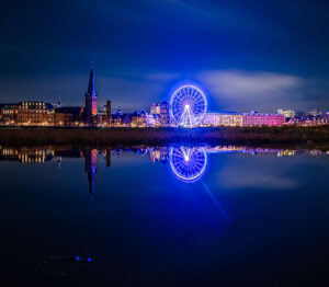 Langzeitbelichtung des beleuchteten Riesenrads bei Nacht in Düsseldorf mit Spiegelung im Rhein – Fine Art Print bei Hochwasser und ruhiger Atmosphäre