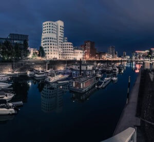 Fine Art Print der Gehry-Bauten im Düsseldorfer Medienhafen mit glasklarer Spiegelung und leuchtender Nachtstimmung in Langzeitbelichtung.