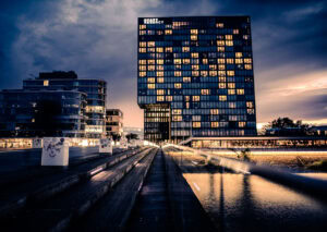 Fine Art Print der Hyatt Regency Skyline Düsseldorf bei dramatischem Abendhimmel mit reflektierendem Wasser und architektonischer Präzision.