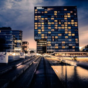 Fine Art Print der Hyatt Regency Skyline Düsseldorf bei dramatischem Abendhimmel mit reflektierendem Wasser und architektonischer Präzision.