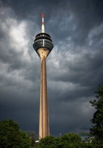 Fine Art Print des Rheinturms in Düsseldorf nach Regenschauer – eine Turmseite sichtbar durchnässt, dramatische Wolken und intensives Nachlicht.