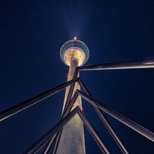 Fine Art Print des beleuchteten Rheinturms in Düsseldorf bei Nacht mit Sternenhimmel, aufgenommen aus einer ungewöhnlichen Perspektive.