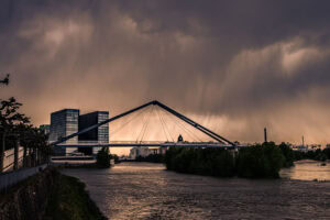 Fine Art Print vom Düsseldorfer Rheinufer mit moderner Brücke bei Gewitterstimmung – dramatische Wolken und Lichtstimmung über dem Rhein.