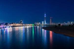 Fine Art Print der Düsseldorfer Skyline bei Nacht mit bunten Lichtspiegelungen im Rhein – moderne Architektur trifft auf stille Flusslandschaft.