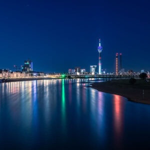 Fine Art Print der Düsseldorfer Skyline bei Nacht mit bunten Lichtspiegelungen im Rhein – moderne Architektur trifft auf stille Flusslandschaft.
