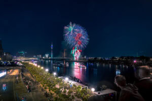 Fine Art Print des Japantag-Feuerwerks in Düsseldorf bei Nacht – farbenprächtiger Himmel über der Rheinuferpromenade mit Lichtern und Menschen.
