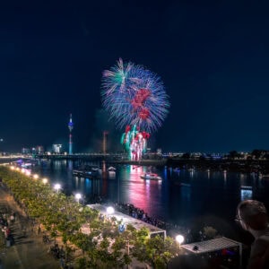 Fine Art Print des Japantag-Feuerwerks in Düsseldorf bei Nacht – farbenprächtiger Himmel über der Rheinuferpromenade mit Lichtern und Menschen.