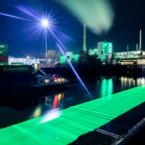 Düsseldorf Industriehafen Lausward – grünes Lichtband über dem Wasser, Laternen-Lichtstern und Rauchfahne, Nacht, Langzeitbelichtung.
