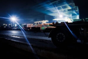 Düsseldorf Industriehafen – Containerterminal bei Nacht mit Lichtspuren, Scheinwerfer-Lichtsternen und Trailer-Silhouette, Langzeitbelichtung.