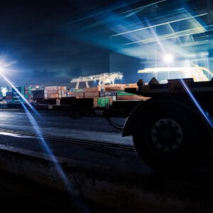 Düsseldorf Industriehafen – Containerterminal bei Nacht mit Lichtspuren, Scheinwerfer-Lichtsternen und Trailer-Silhouette, Langzeitbelichtung.