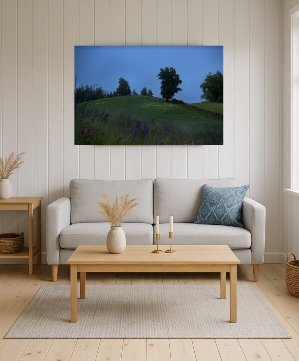 Helles skandinavisches Wohnzimmer mit Holzboden und weißer Lamellenwand; an der Wand ein Foto „Oberbozen im Regen“ mit Blumenwiese, altem Zaun und Wald im Nebel, Blaue Stunde.