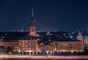 Tele-Nachtaufnahme der Riddarholmskyrkan auf Riddarholmen, Stockholm; beleuchtete Dächer und dezente Lichtspuren vor dunklem Himmel.