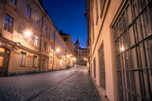 Beleuchtete Kopfsteinpflaster-Gasse in Stockholm-Södermalm mit Blick zur Katarina kyrka bei Nacht; Laternen mit Stern-Effekten, warme Fassaden.