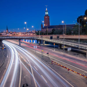Stadtansicht mit Stockholms Stadshuset, Centralbron und hellen Autolichtspuren bei blauer Stunde; Laternen als Sterne, Mondsichel am Himmel.