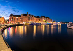 Panorama Strandvägen Stockholm bei Nacht, reflektierte Lichter der Fassaden und Boote im ruhigen Wasser.