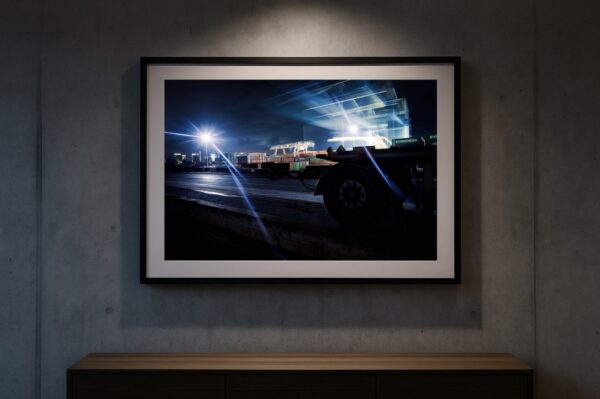 Gerahmter Fine-Art-Print des Düsseldorfer Industriehafens mit Lichtspuren des Hafenkrans an Beton-Galeriewand unter Spotbeleuchtung.