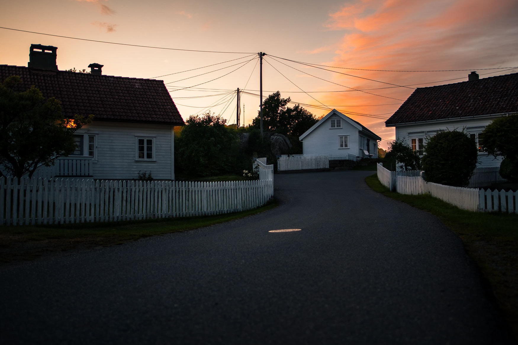 Ruhige Dorfstraße mit weißen Holzhäusern bei Sonnenuntergang