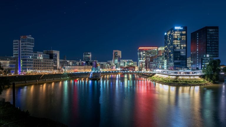 Nachtpanorama des Düsseldorfer Medienhafens mit bunt beleuchteten Hochhäusern und Reflexionen im Wasser