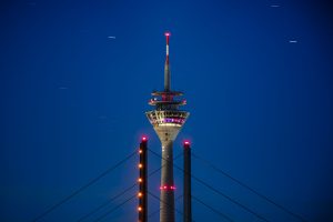 Beleuchteter Fernsehturm hinter Brückenpylonen vor tiefblauem Nachthimmel