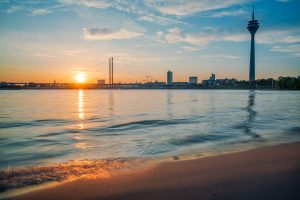 Sonnenaufgang über Düsseldorf mit Rheinturm, Rheinbrücke und ruhigem Sandstrand