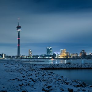 Verschneite Rheinuferwiesen mit Düsseldorfer Rheinturm und Skyline bei Nacht