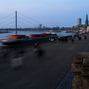 Langzeitbelichtung der Düsseldorfer Rheinuferpromenade mit Frachtschiff bei Abendlicht