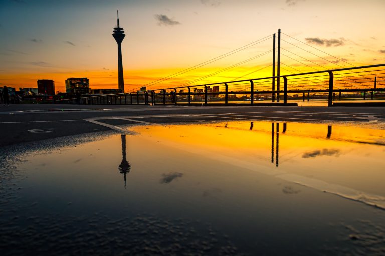 Sonnenuntergang am Düsseldorfer Rheinufer mit Fernsehturm und Brücke, gespiegelt in einer Pfütze