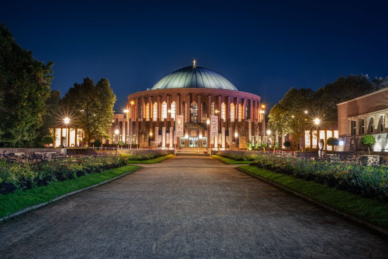 Nachtaufnahme der beleuchteten Tonhalle in Düsseldorf mit Weg und Blumenbeeten