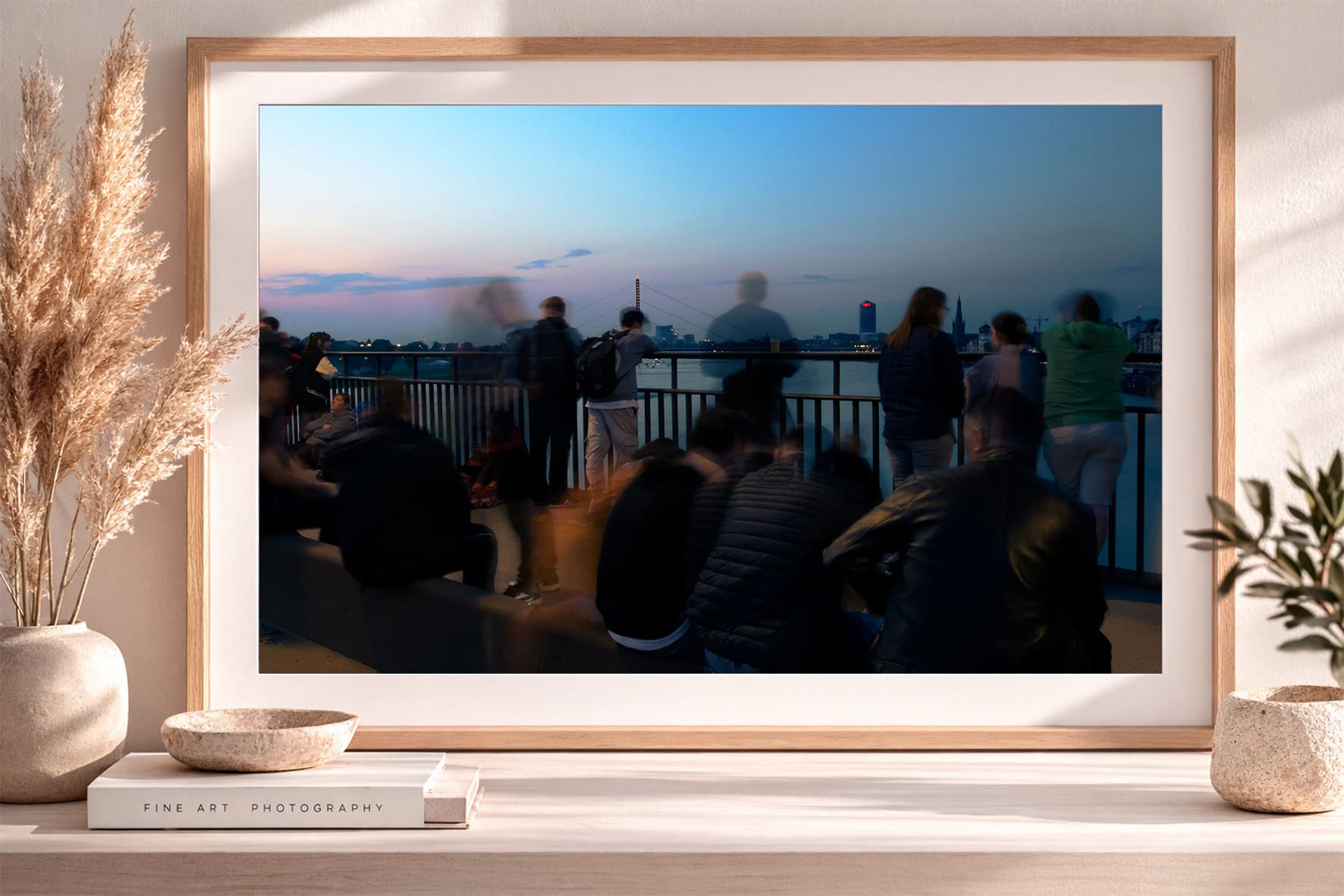 Fotografie von Menschen an einer Brüstung mit Flussblick bei blauem Abendhimmel, gerahmt auf einem Sideboard mit Deko