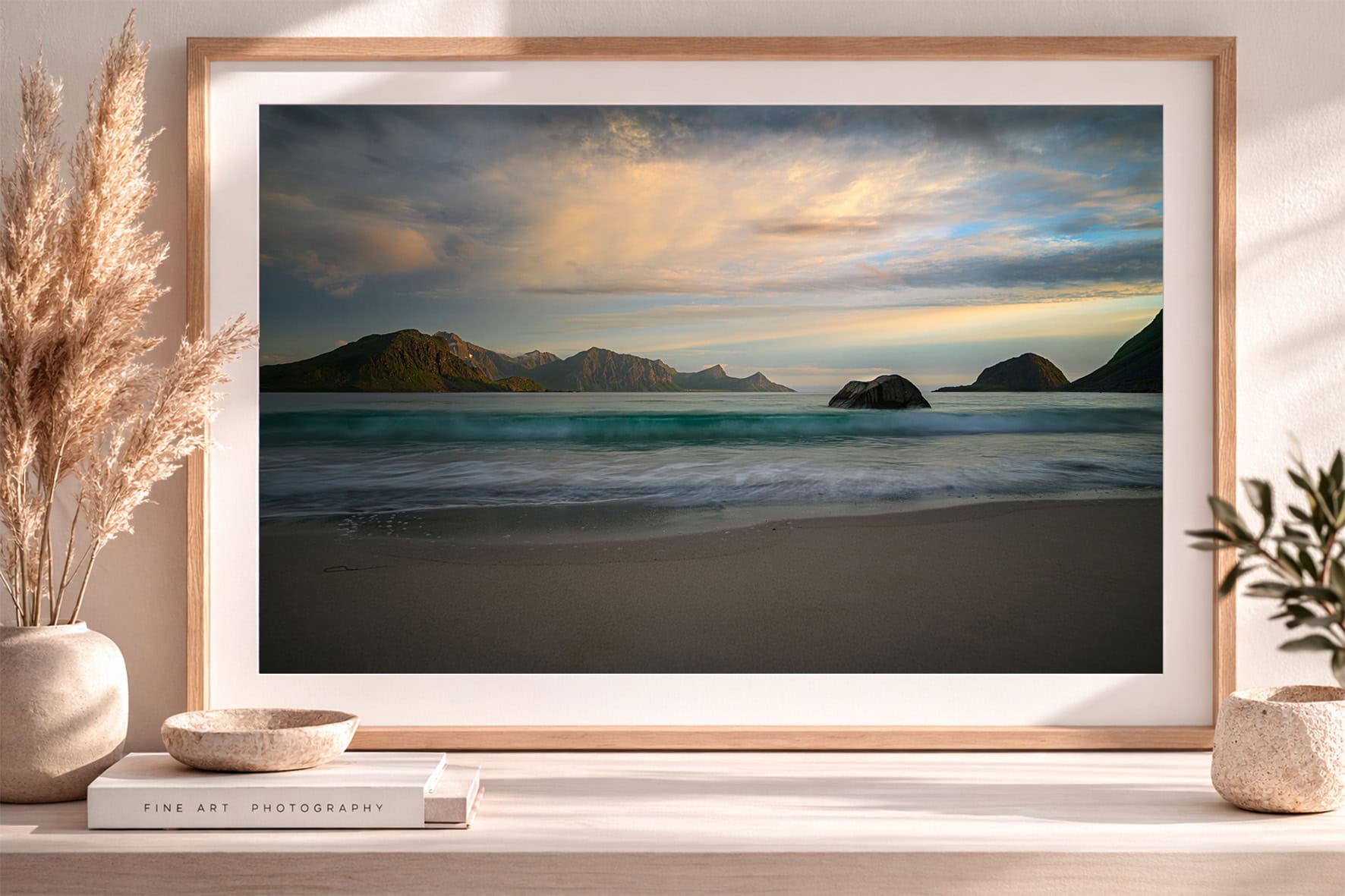 Gerahmter Fotokunstdruck mit ruhigem Strand, türkisfarbenem Meer, Felsen und Bergkette im warmen Abendlicht in hellem Interior