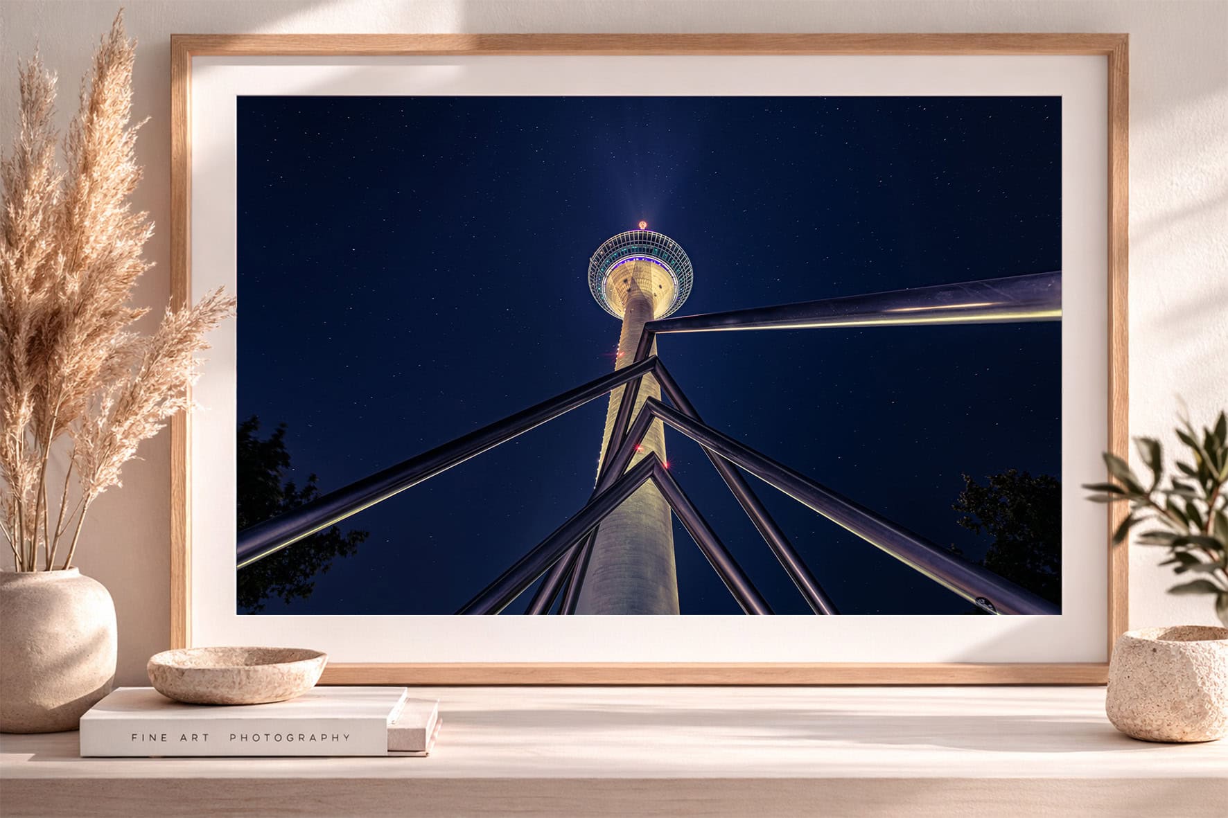 Fotografie eines hell beleuchteten Fernsehturms bei Nacht, von unten mit Stahlstreben aufgenommen, in hellem Rahmen auf Sideboard