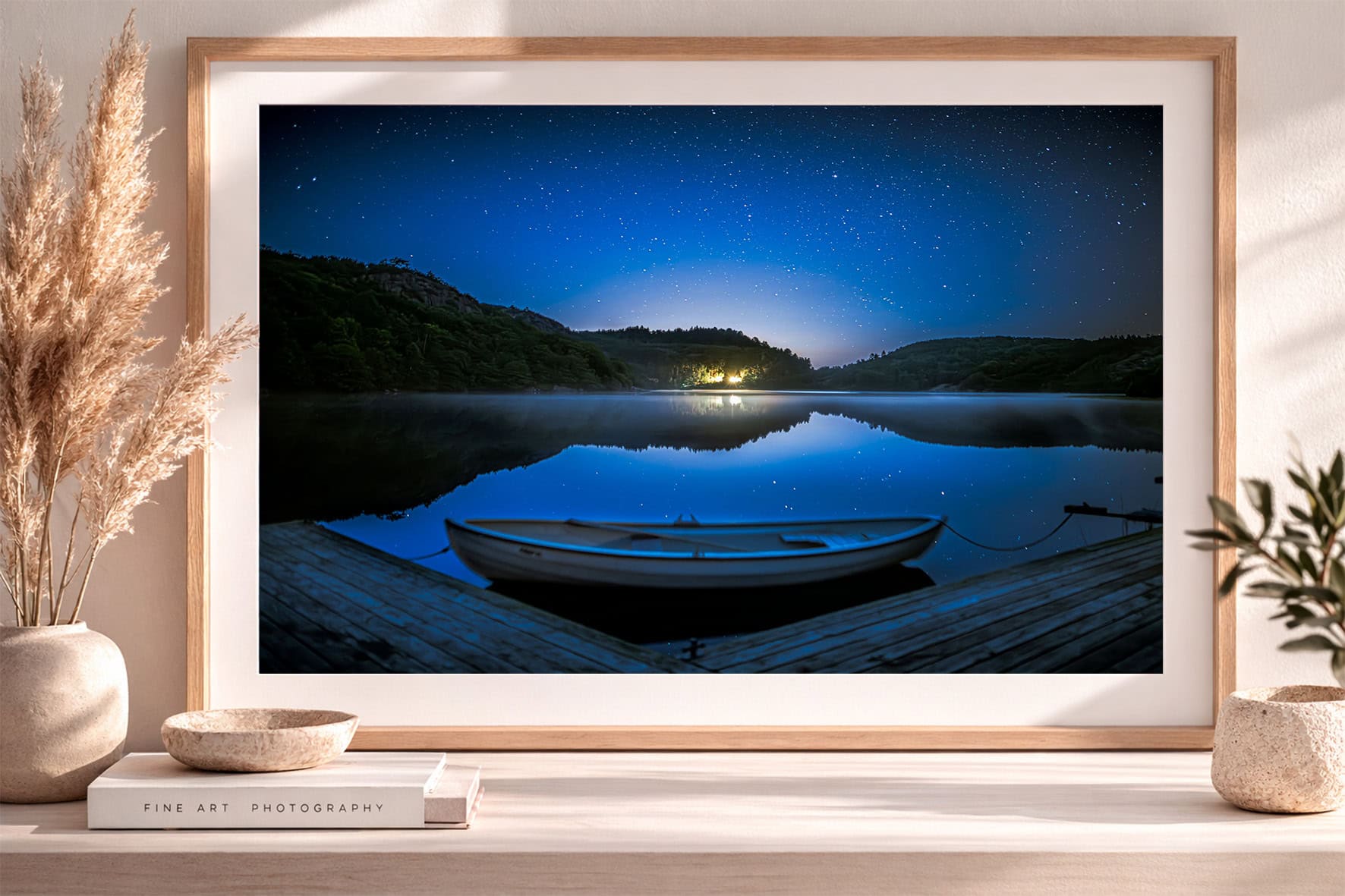 Fotografie eines Ruderboots an einem Steg vor stillem See bei Nacht, klarer Sternenhimmel und ferne Lichter, gerahmt im modernen Interior