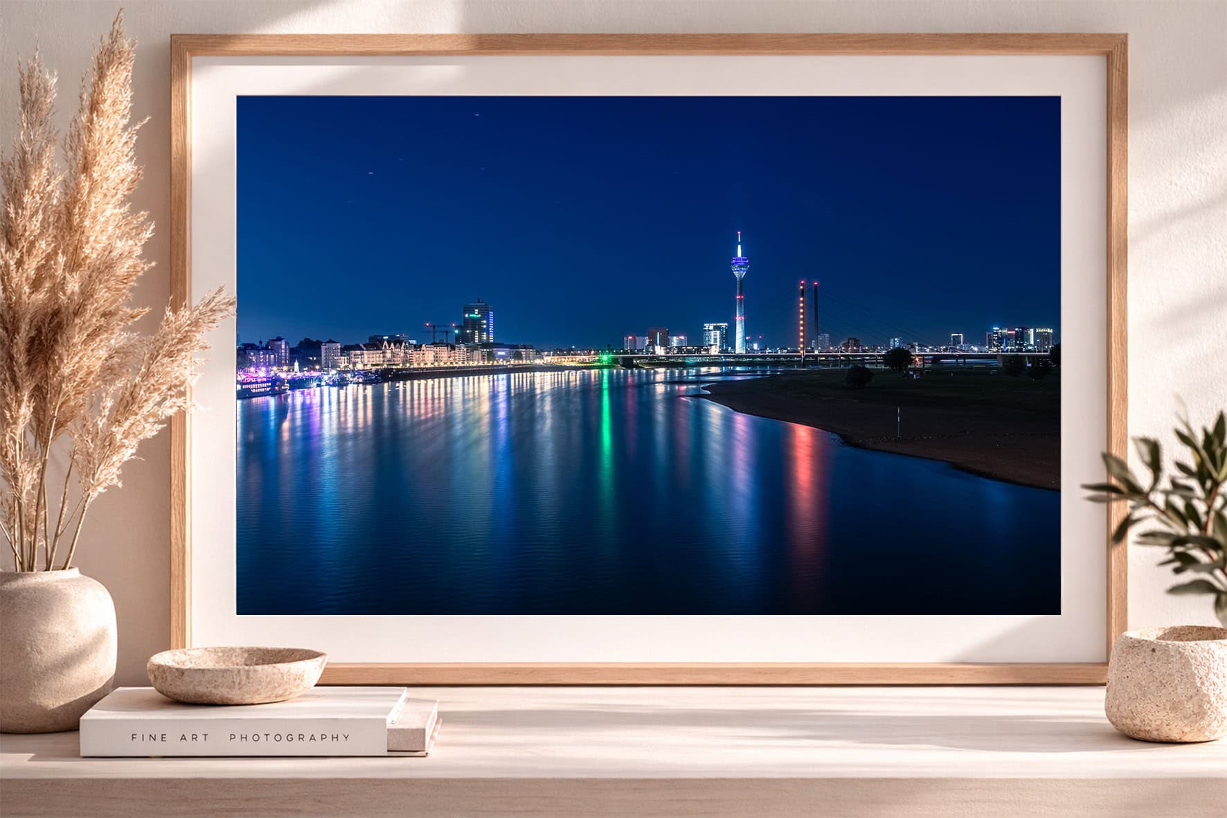 Fotografie einer nächtlichen Skyline mit beleuchteter Brücke und farbigen Lichtreflexen im Fluss, gerahmt auf Sideboard mit Deko