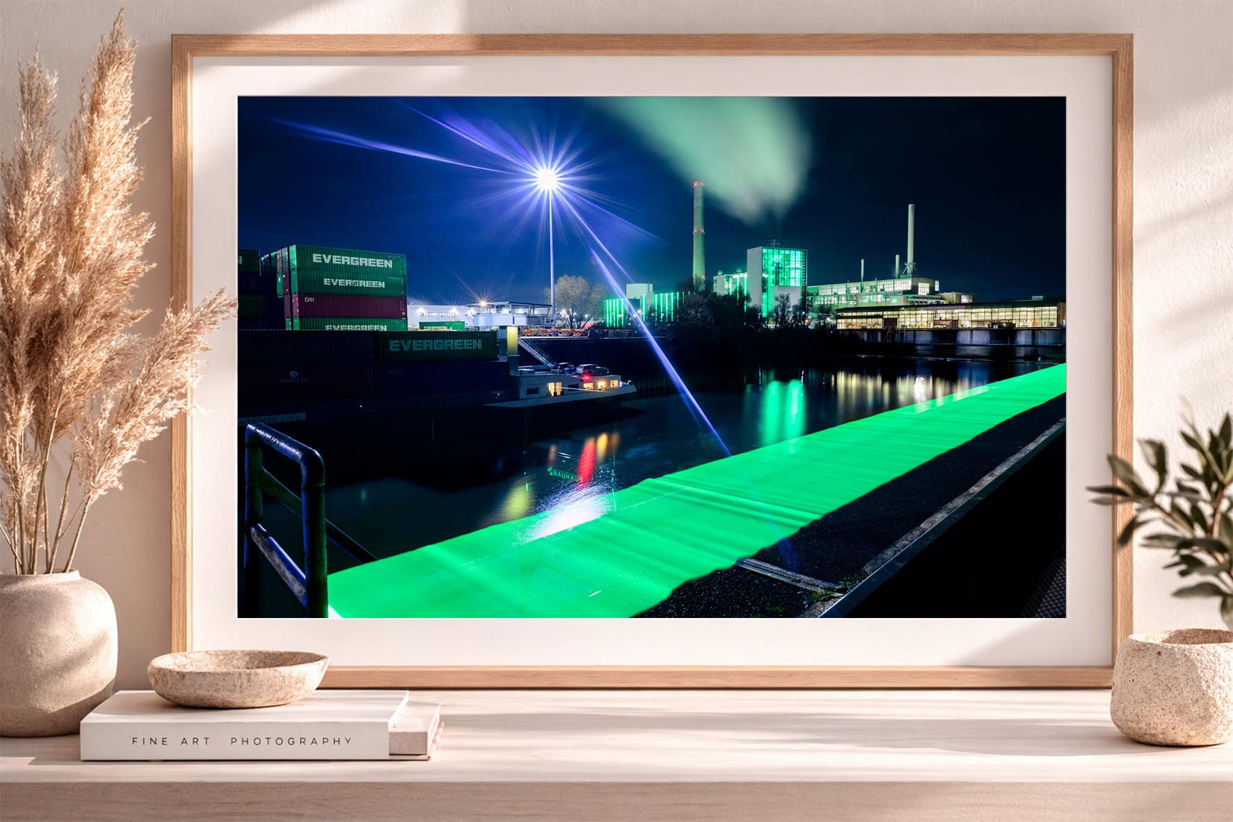 Fotografie eines nächtlichen Industriehafens mit Containern, Schornsteinen und leuchtend grüner Lichtspur am Wasser in Bilderrahmen