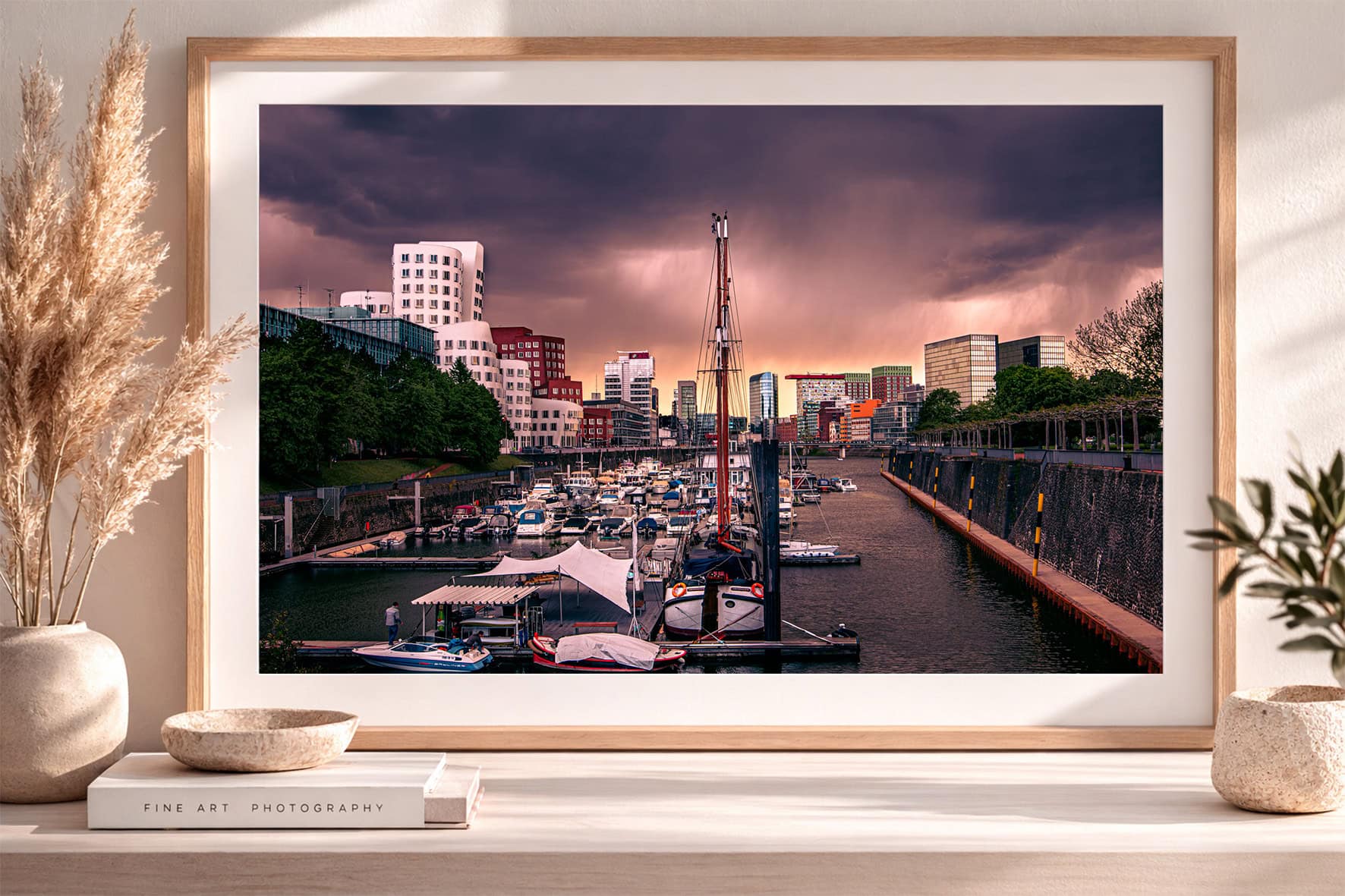 Fotografie eines Stadthafens mit Booten, moderner Skyline und dramatisch warmem Abendhimmel im Holzrahmen auf Sideboard.