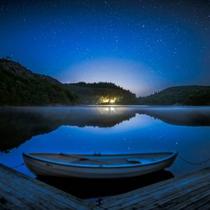 Ruhiger See bei Nacht mit Boot im Vordergrund und klarem Sternenhimmel