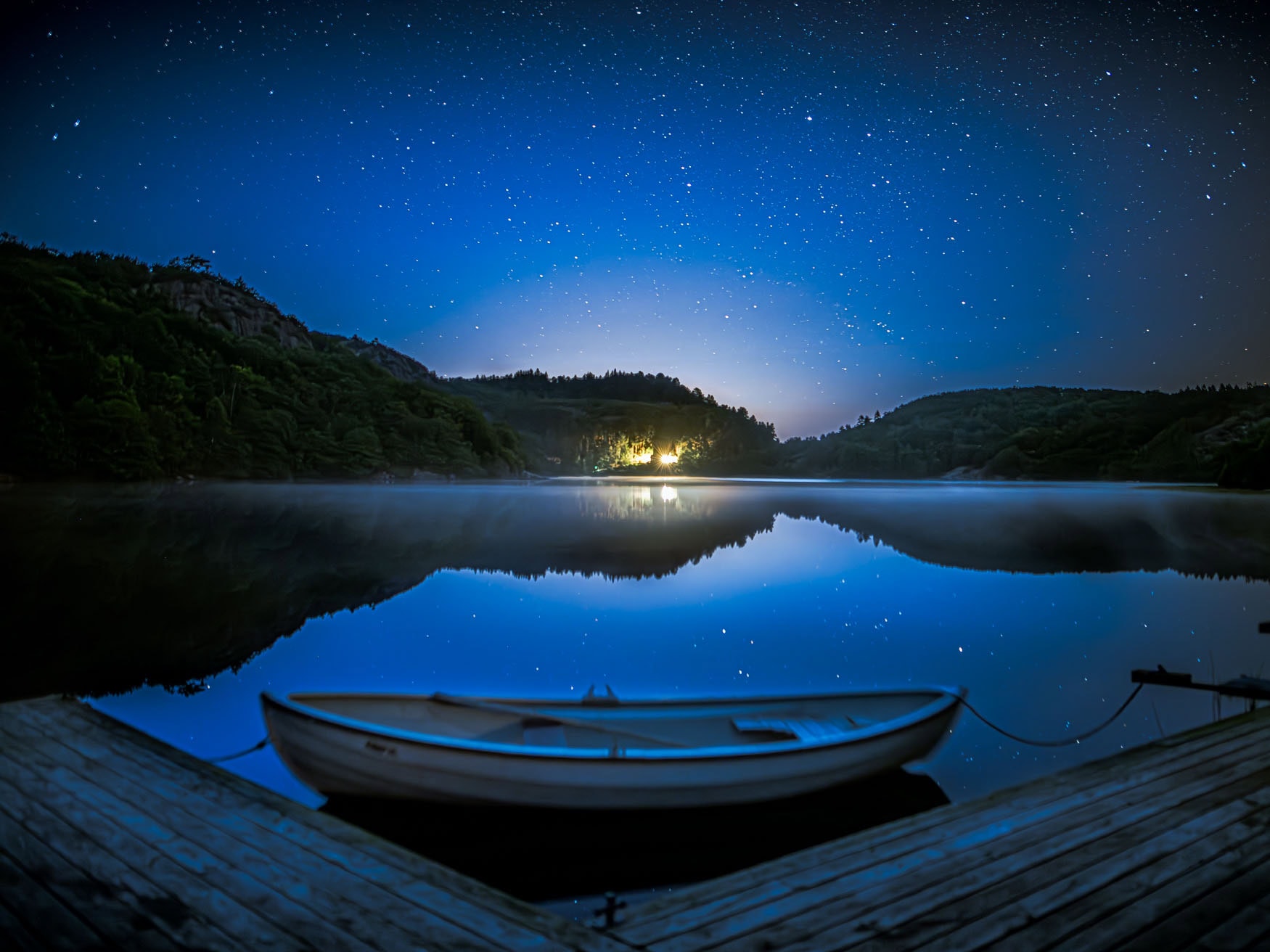 Ruhiger See bei Nacht mit Boot im Vordergrund und klarem Sternenhimmel