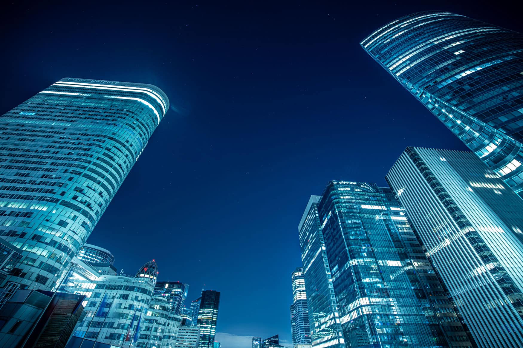 Blick nach oben auf beleuchtete Hochhäuser in Paris La Défense bei Nacht mit abstrakter Perspektive