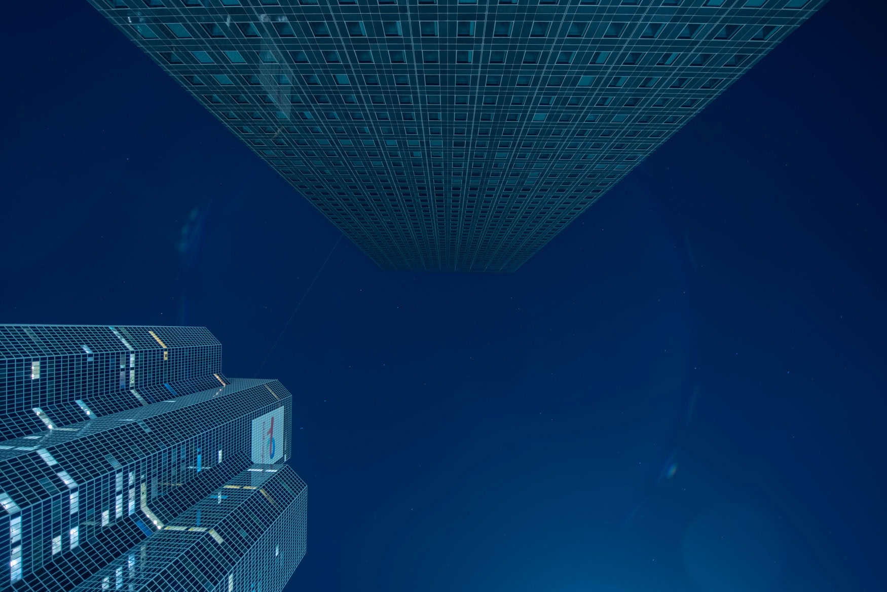 Blick nach oben auf zwei Wolkenkratzer in Paris La Défense bei Nacht vor tiefblauem Himmel