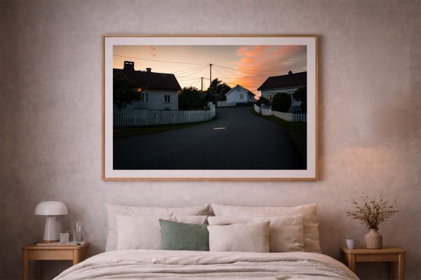 Fotografie einer kurvigen Dorfstraße mit weißen Holzhäusern bei Sonnenuntergang, als gerahmtes Wandbild über einem Bett im Schlafzimmer