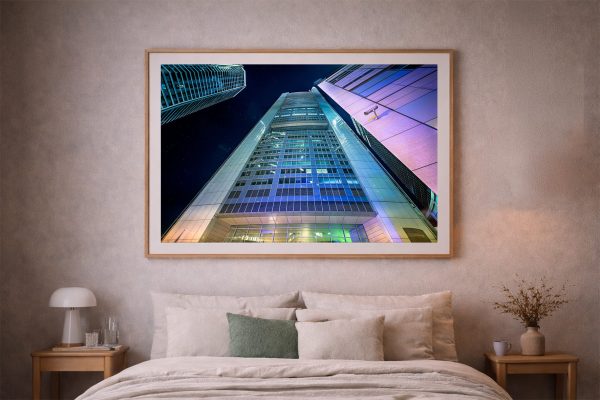Fotografie eines beleuchteten Hochhauses bei Nacht im Holzrahmen über einem Bett in einem modernen Schlafzimmer