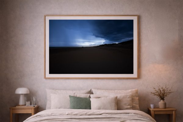 Großes Wandbild mit dunkler Strandlandschaft und blauem Abendhimmel über einem beige eingerichteten Schlafzimmer