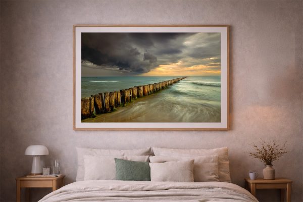 Großer gerahmter Fotodruck mit Holzpfahl-Reihe im Meer unter dramatischem Himmel über einem Bett im gemütlichen Schlafzimmer.
